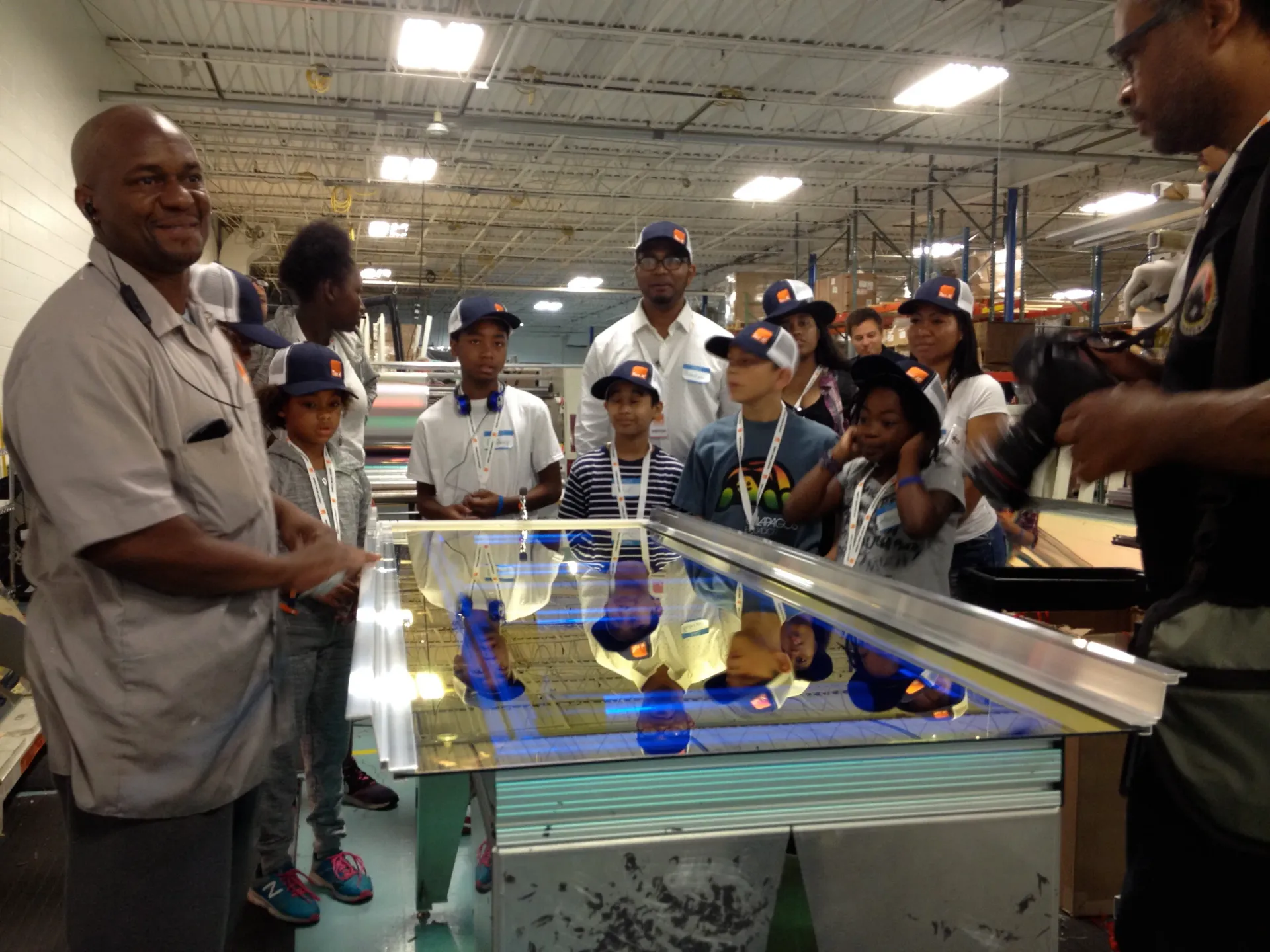 A school group visiting a warehouse stand around a table with a solar panel lying on it.