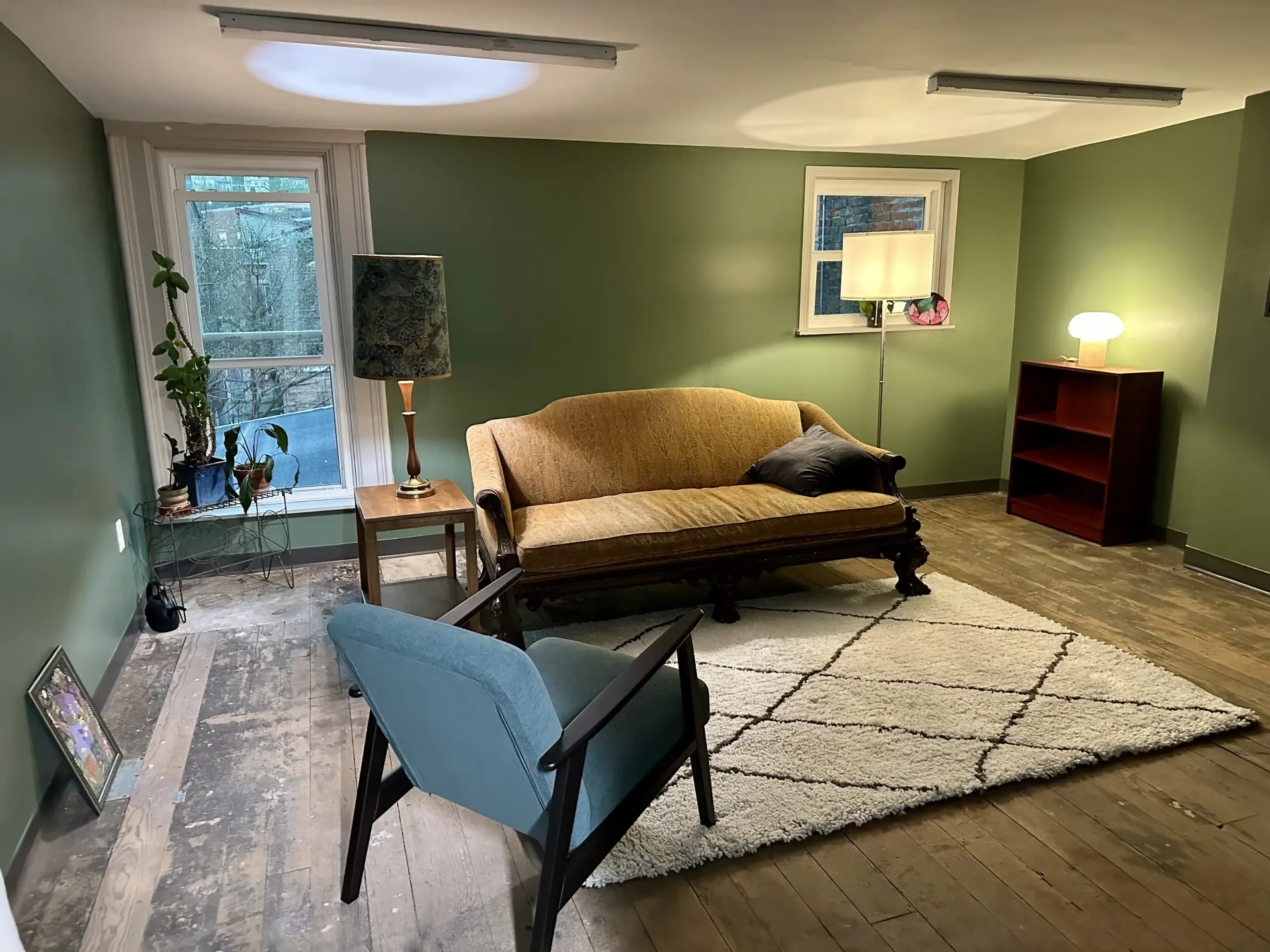 A therapist's office with green walls, soft yellow light, a tan couch and blue chair